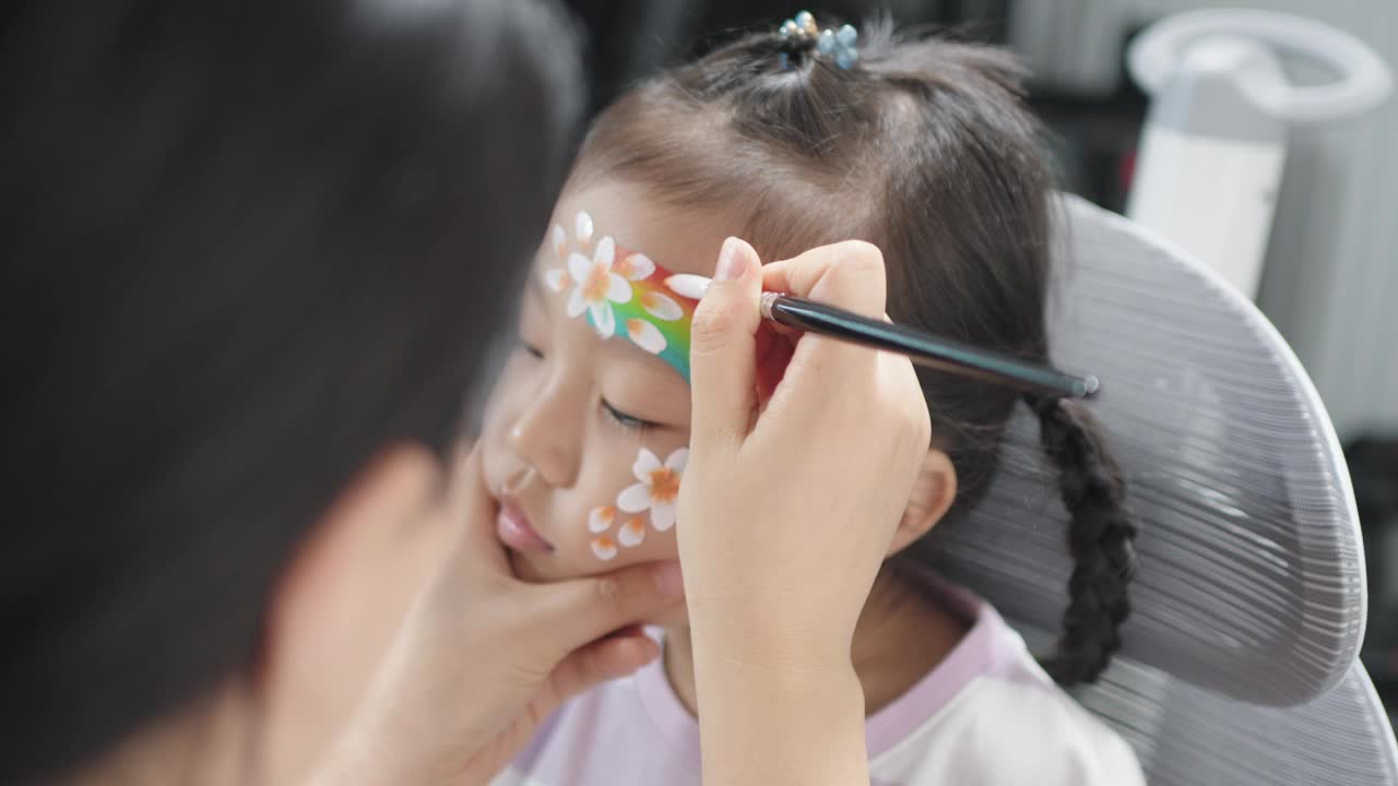 一位亚洲妇女正在给她的小女儿脸上画画视频下载