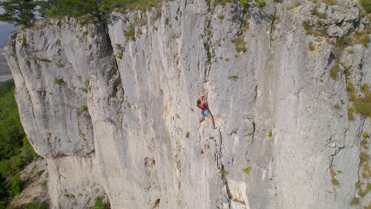 航拍:年轻的攀登者在石灰岩岩壁上接近攀爬路线的顶端视频下载