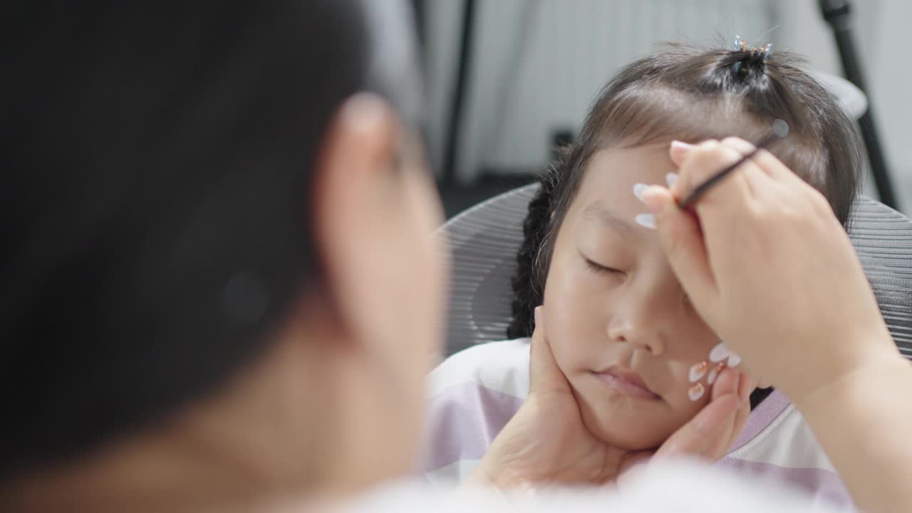 一位亚洲妇女正在给她的小女儿脸上画画视频下载