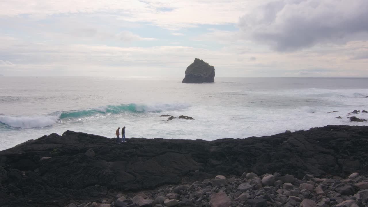 冰岛雷克雅那，两名男子走在岩石嶙峋的海岸线上，伴随着破碎的海浪视频下载