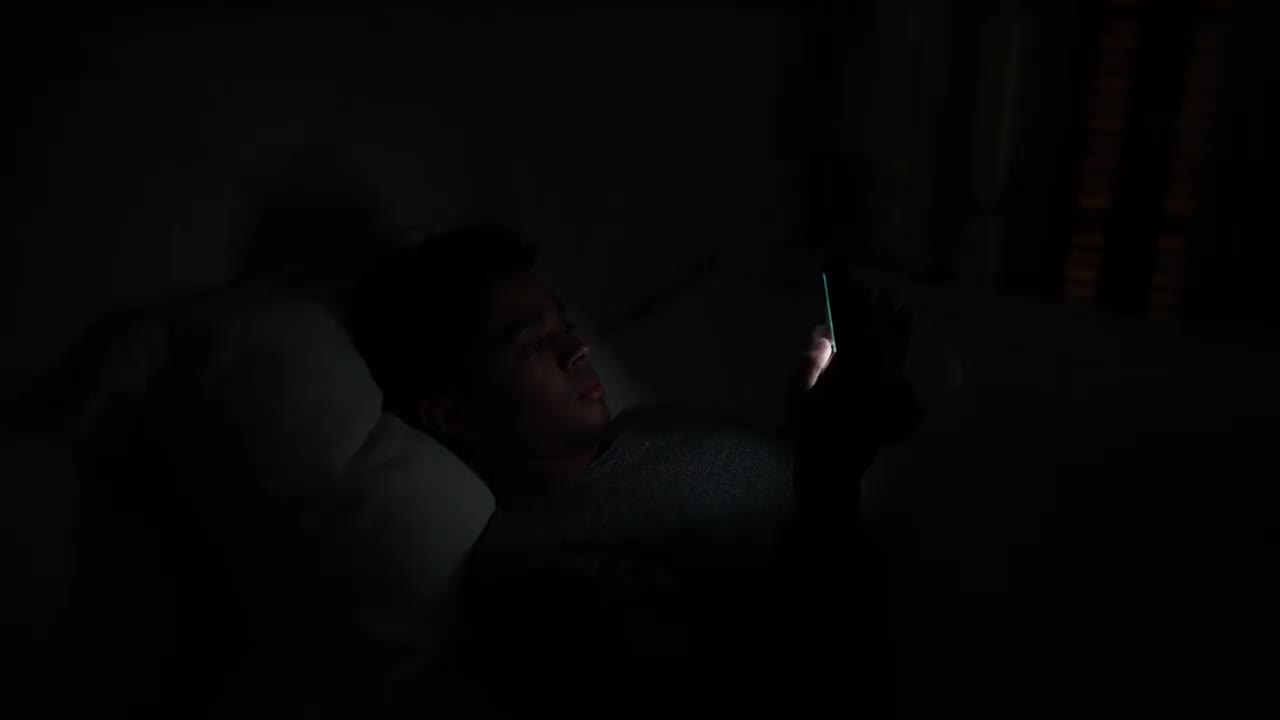 年轻人在家里的床上玩智能手机视频下载