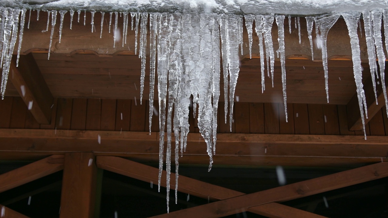 冰柱挂在木屋的屋顶上，飘落着雪花。冬季圣诞节的节日气氛。视频素材