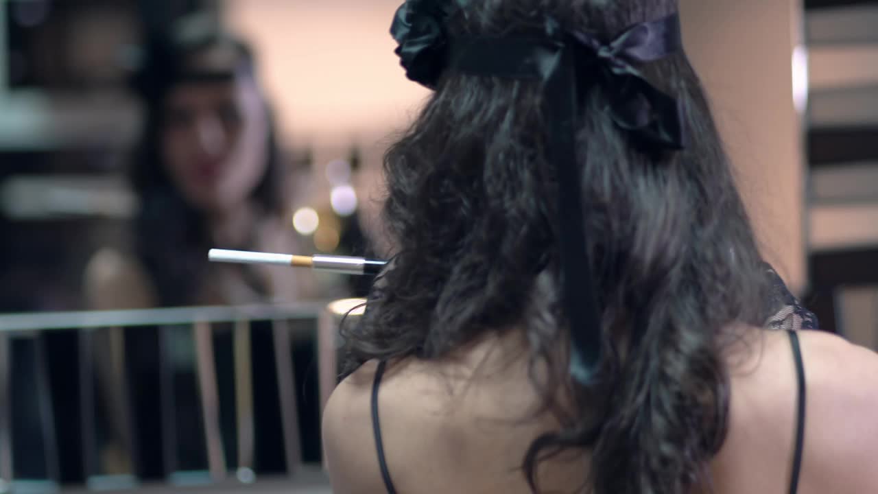 性感微笑的女人穿着20年代《了不起的盖茨比》的风格，在一个主题派对上抽烟。身穿黑色连衣裙，戴着珍珠项链，留着复古的发型。视频下载