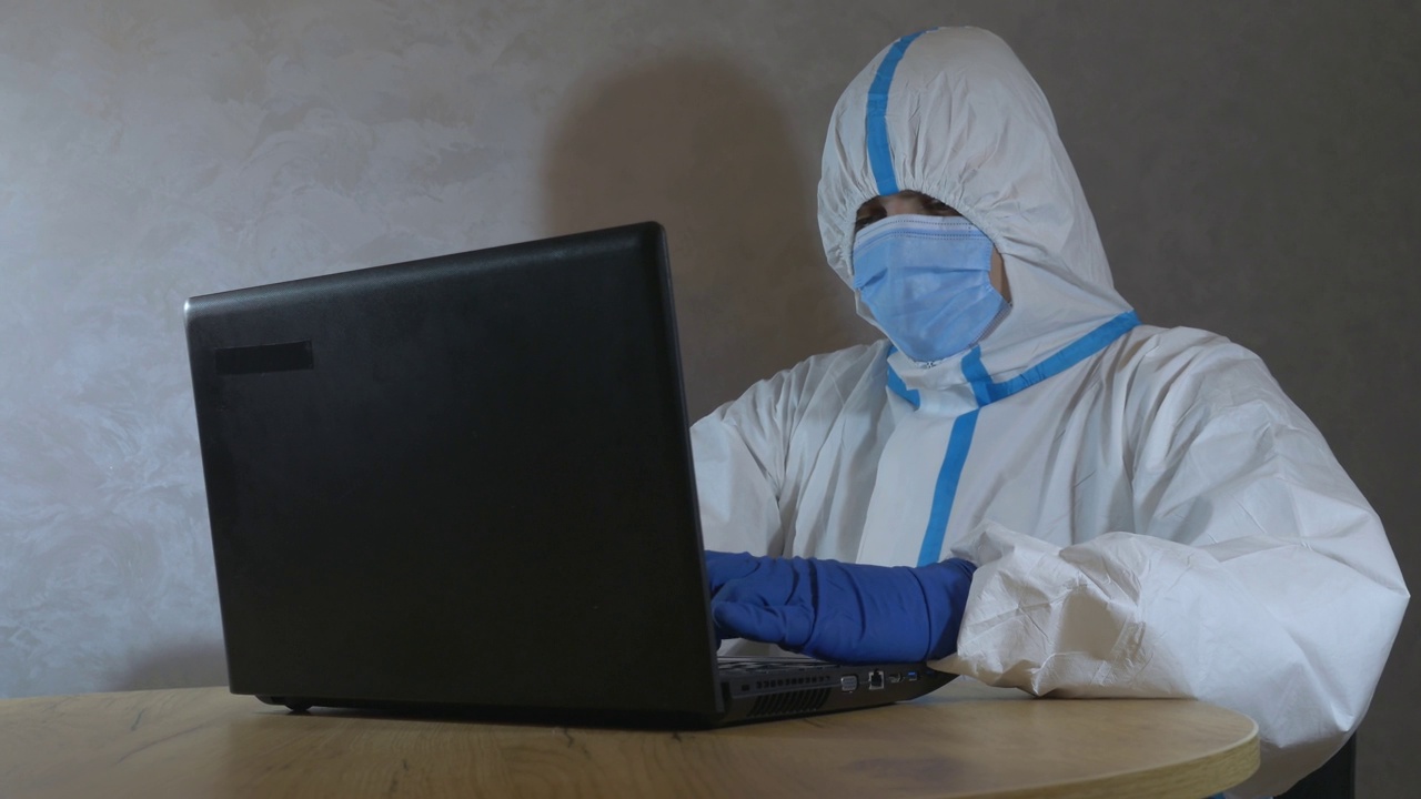 医生穿着医疗防护服，戴着医用口罩和手套，在笔记本电脑上工作。病毒流行保护mers。冠状病毒(COVID-19)。医疗保健的概念。大流行疫情下的远程工作。视频下载