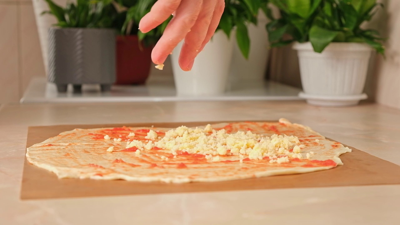 一名男子将马苏里拉奶酪洒在一层酵母面团上，这是披萨的基础。自制披萨。视频素材