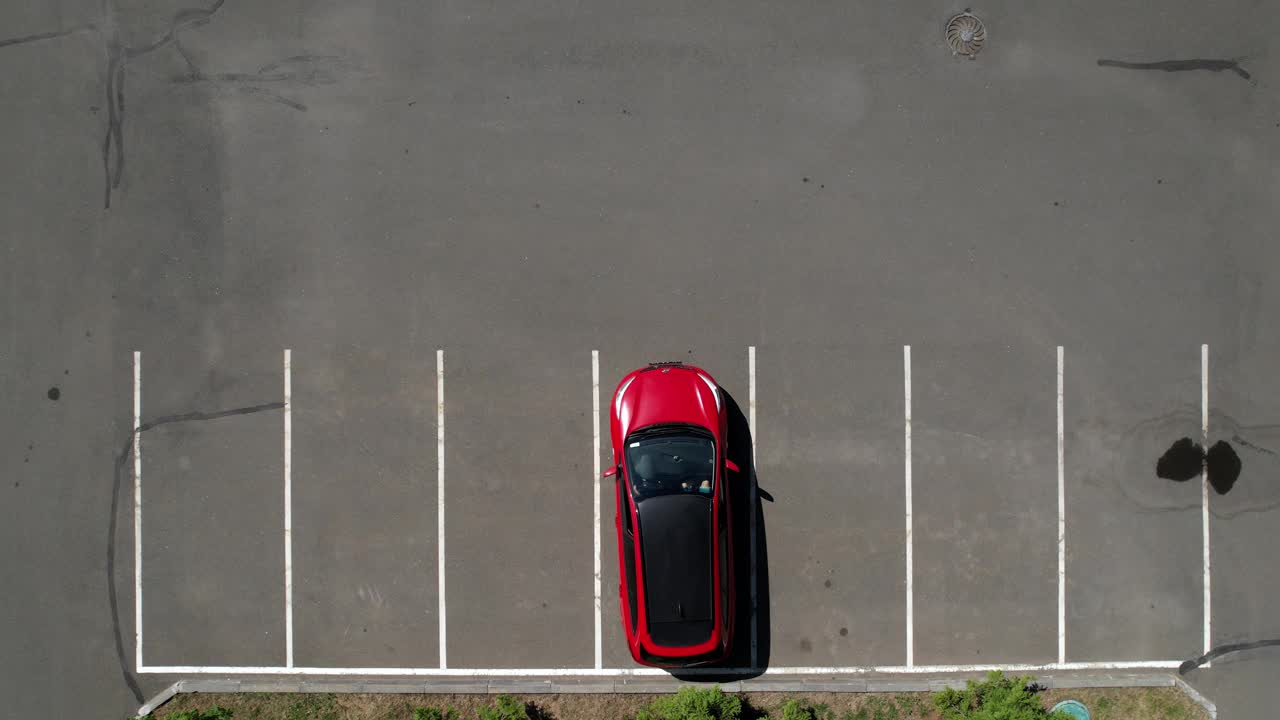 一辆红色轿车从停车场驶出，开走了，航拍画面。空荡荡的停车场。停车场有光滑的白色斑纹。车停好了，俯视图。视频下载