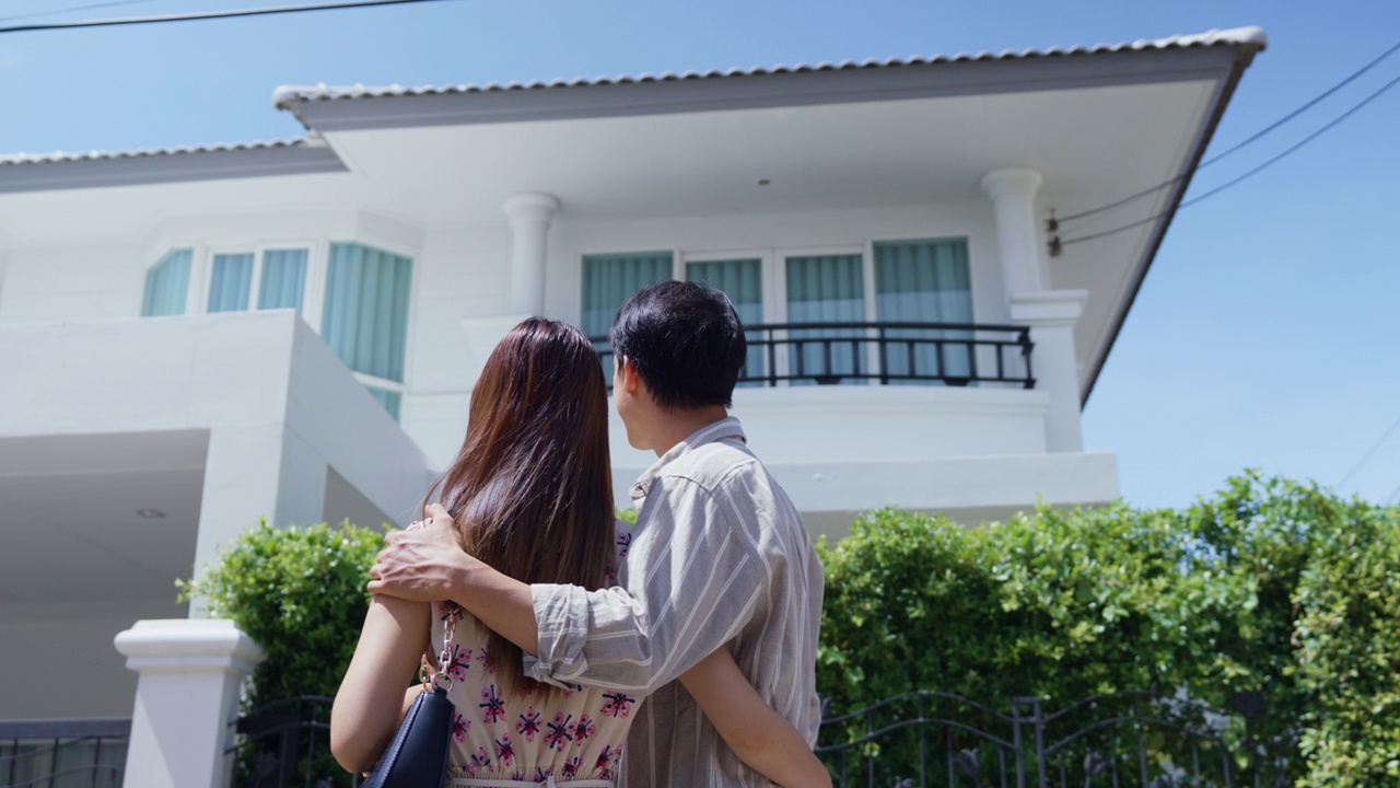 亚洲年轻夫妇拥抱并看着对方，庆祝他们搬进了新房子。视频下载