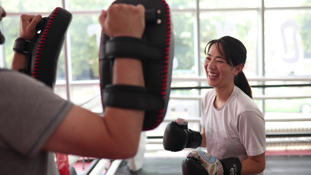 年轻的亚洲女子在拳击馆与男教练一起训练视频下载