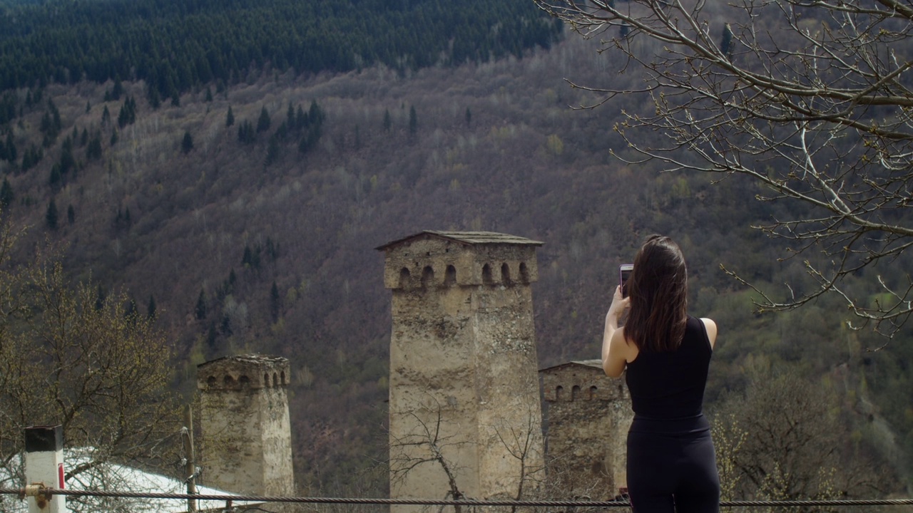 年轻女子在山上拍摄古老的石塔。斯瓦涅季传统的古格鲁吉亚建筑景观。文化遗产视频下载