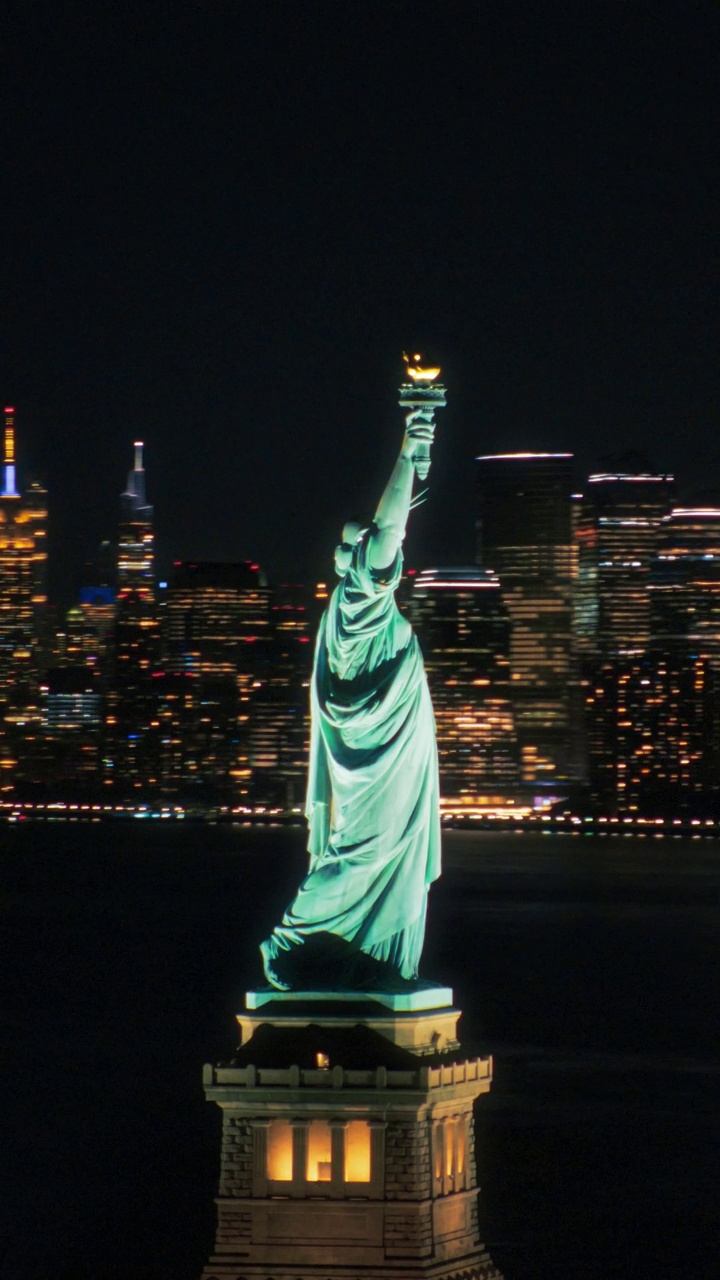 垂直屏幕:空中直升机电影的自由女神像与曼哈顿天际线城市景观与灯光在办公大楼在晚上。纽约天际线全景视频下载