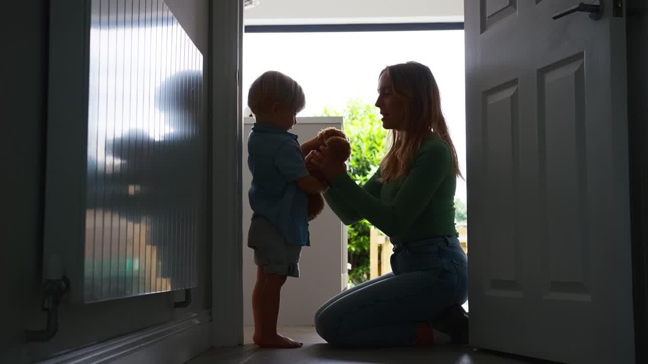 慈爱的母亲在厨房里抱着年幼的儿子，明亮的窗户映衬出她的身影视频素材