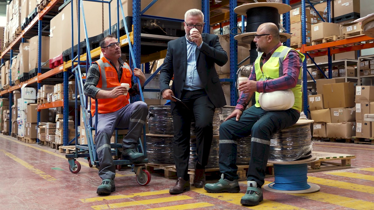 一群男工人，蓝领工人和业务经理，在工厂仓库的换班休息时间拿着咖啡杯吃早餐，聊天视频下载