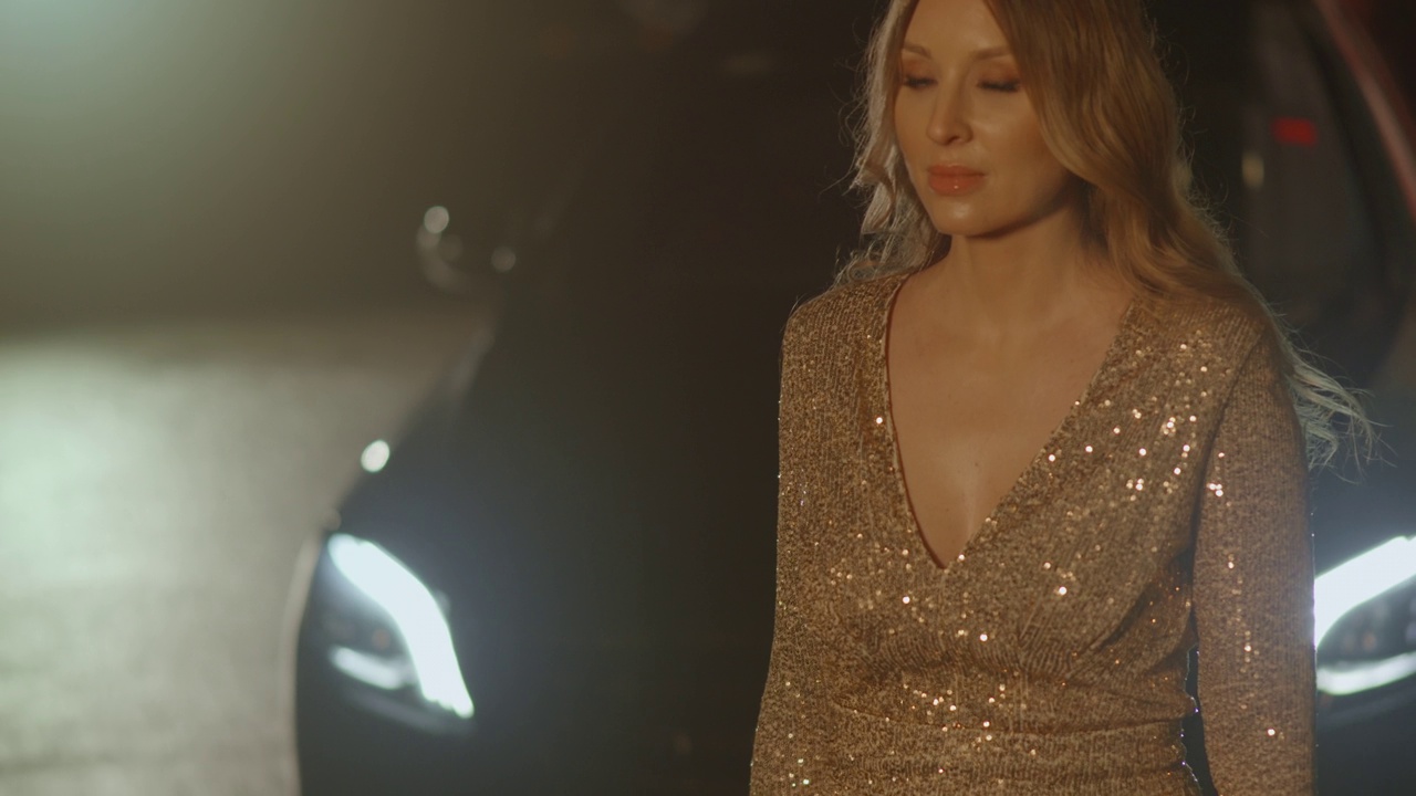 美丽的豪华女子在汽车灯光下慢慢走，晚上的活动视频下载