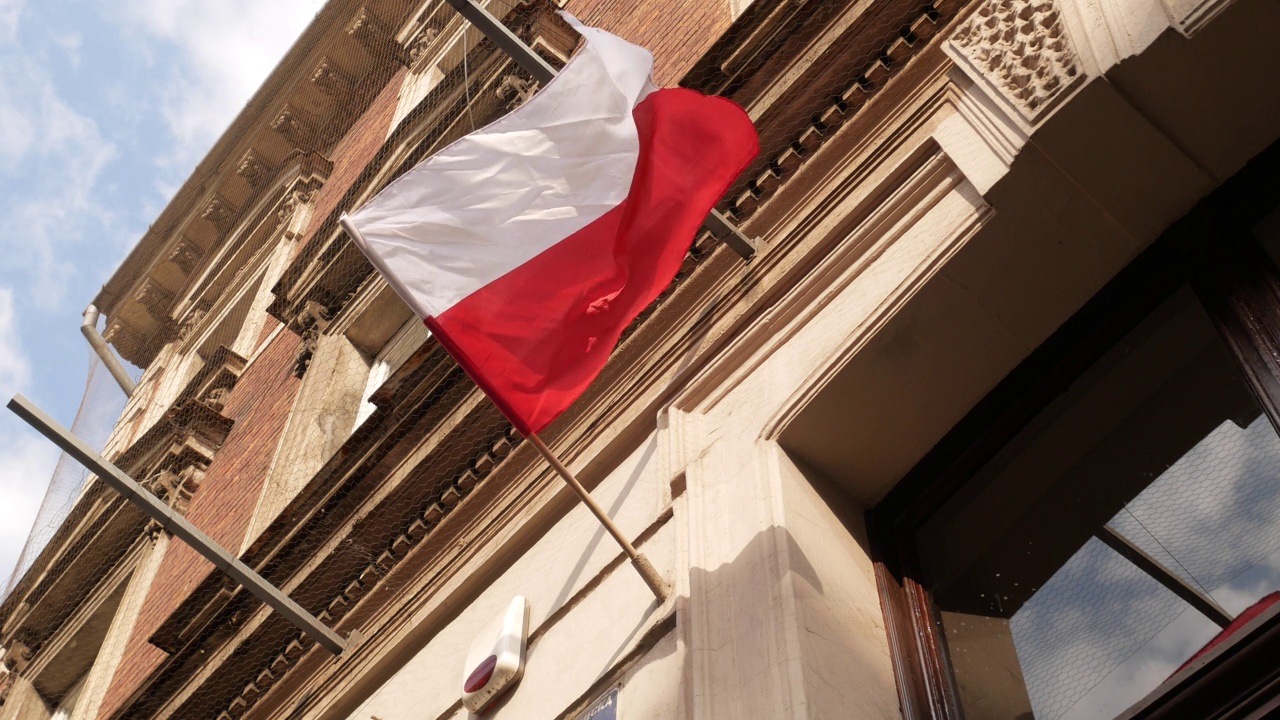 波兰国旗飘扬在杆子上，在建筑的墙上。波兰共和国红白相间的旗帜。视频下载