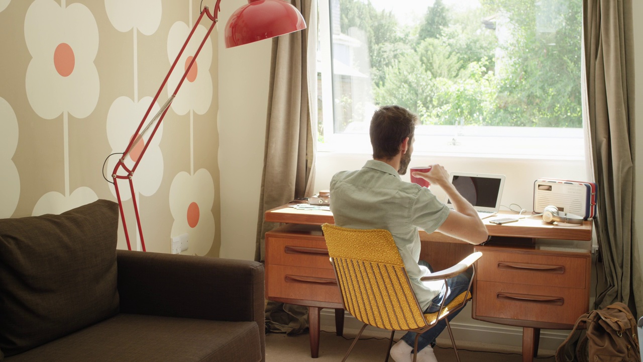 在复古时尚的家庭办公室里，男子在办公桌前使用智能手机平板电脑工作视频下载