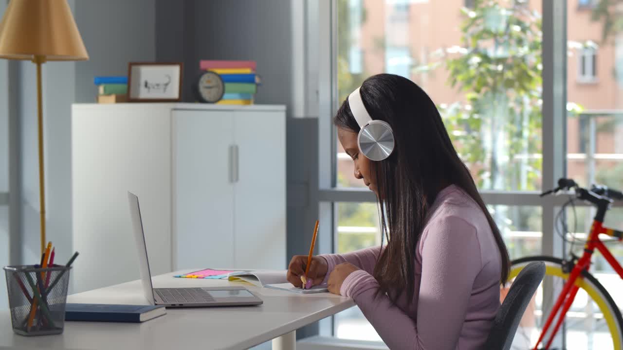 专注的非裔美国少女戴着耳机写笔记用笔记本电脑学习视频下载