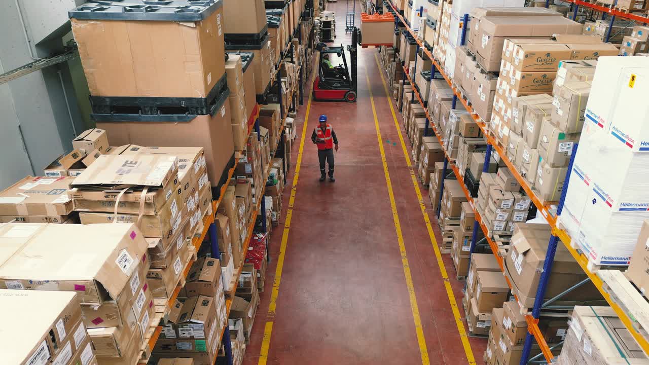 身穿制服的工人在工厂仓库用叉车装载机驾驶和装载纸箱的鸟瞰图视频下载