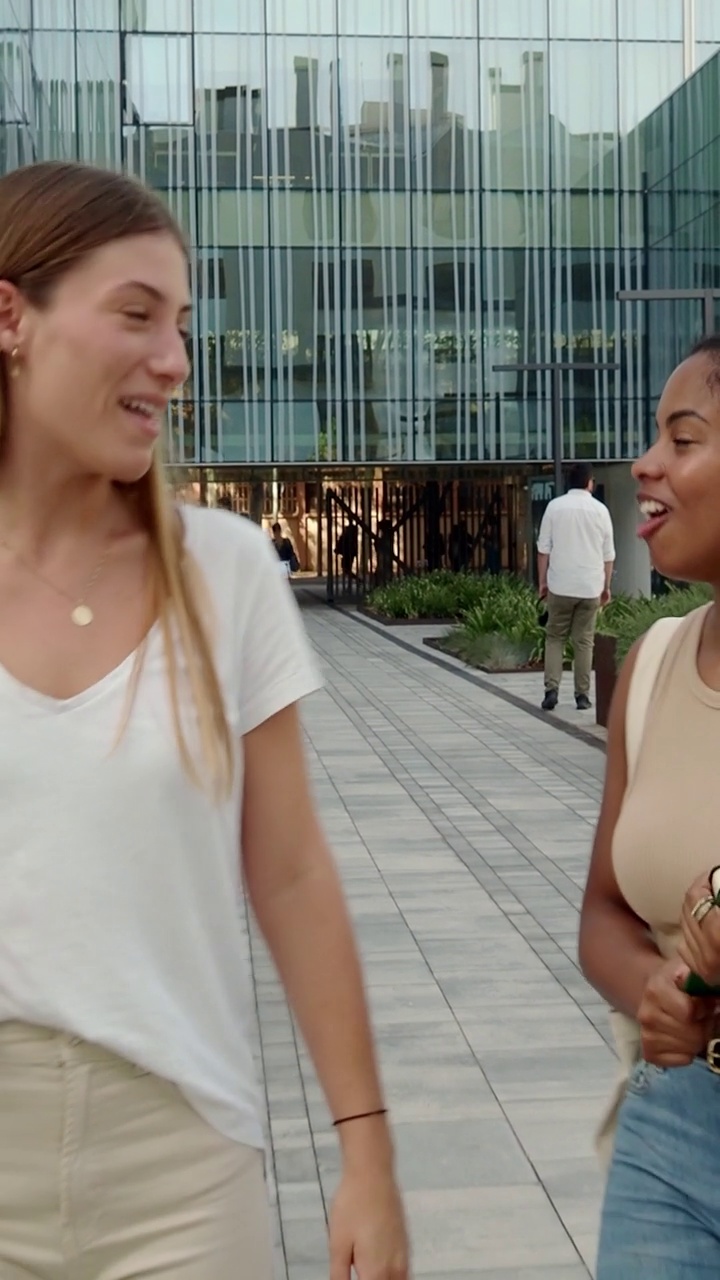 垂直视频。两个不同的十几岁的女学生拿着文件夹在校园里散步聊天视频素材