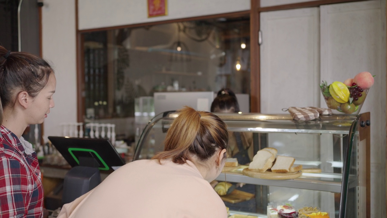 在咖啡店里，漂亮的店主正在为两位挑选烘焙食品的年轻女顾客服务。小企业，企业主。视频素材
