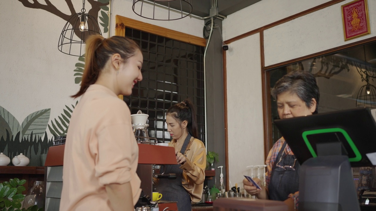 顾客用信用卡付餐费。亚洲可爱的老人，老人，退休，女人。母亲和女儿在她的咖啡店工作。视频素材