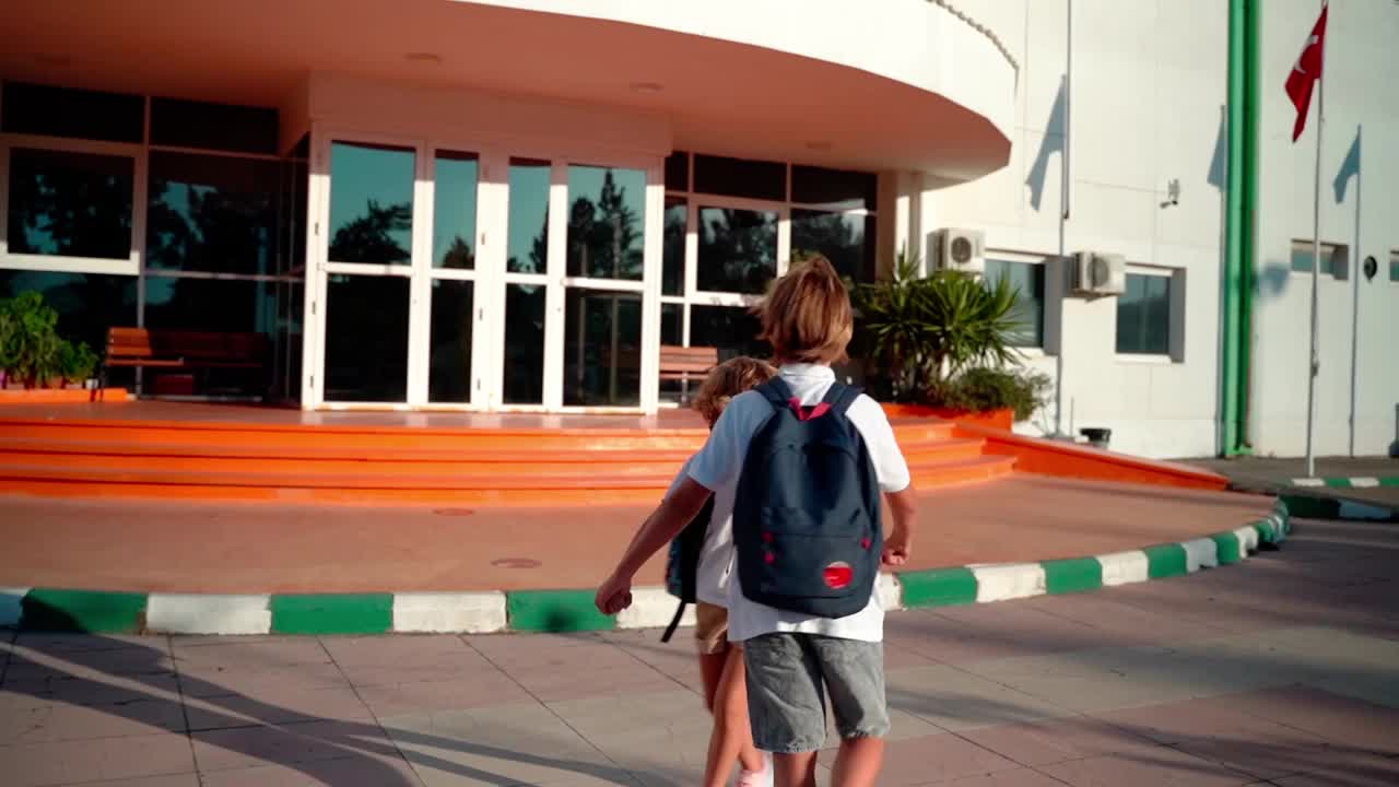 课间休息时，学生和孩子背着书包在院子里玩纺纱。回到学校。小学班教育。手牵着手开心地跑着笑着。后视视频素材