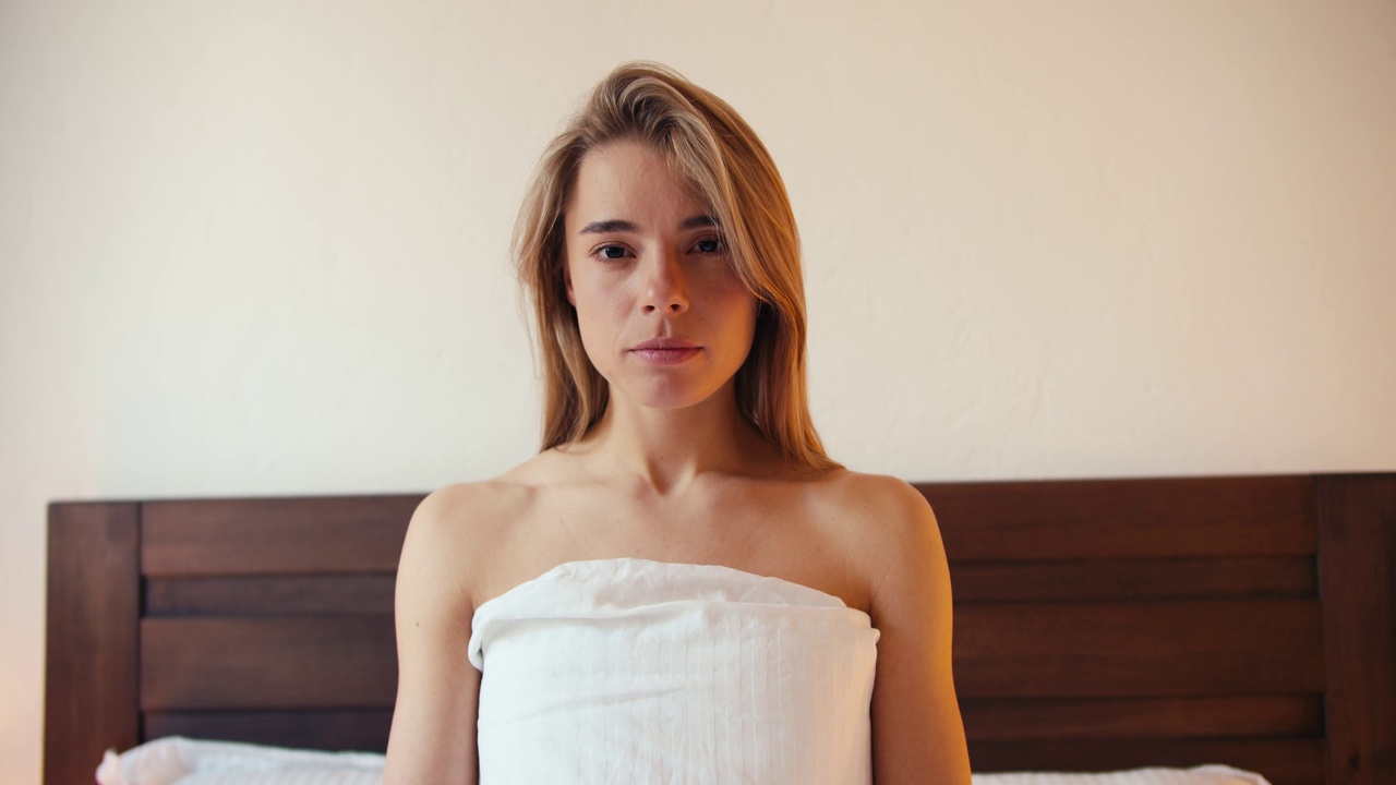 一个金发女孩闭着眼睛坐在床上冥想的肖像。视频拍摄的高质量视频素材