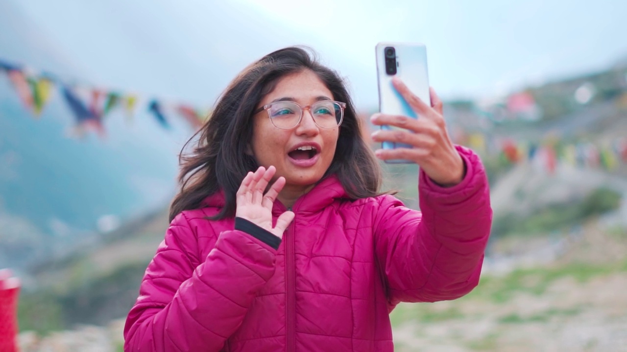 激动的年轻印度女子在视频通话中表情生动的肖像。女孩用智能手机和家人联系。游客在山里拍视频。视频下载