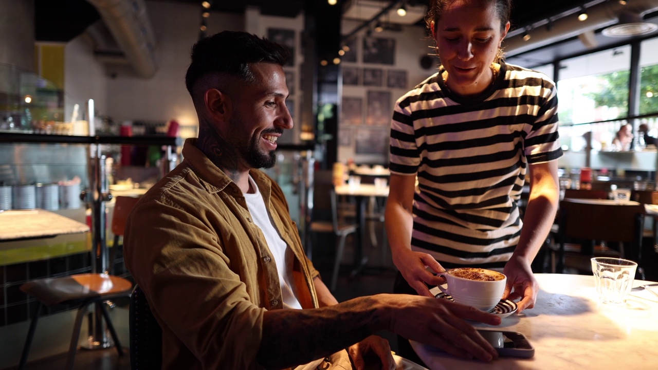 好心的女服务员把咖啡端到正在看智能手机的西班牙裔男子面前视频下载
