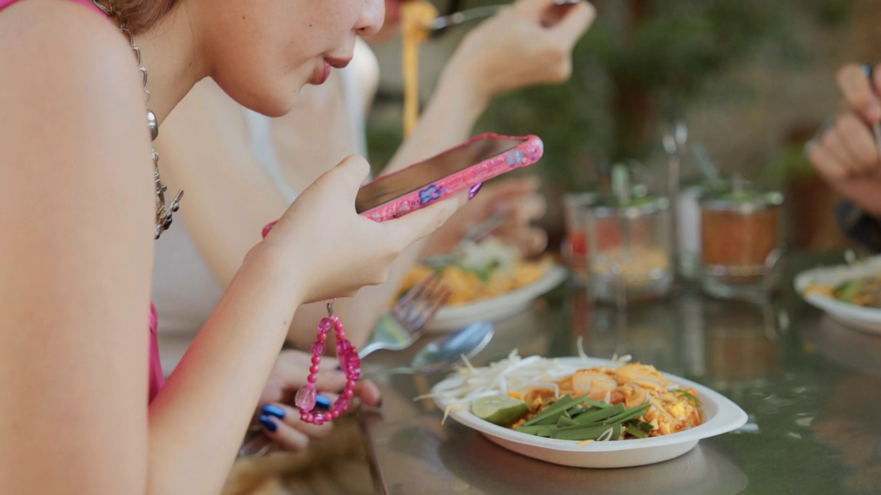 年轻漂亮的女人和她的朋友在当地市场享受美食。她在吃饭前用手机给她的朋友们拍了张照片。视频下载