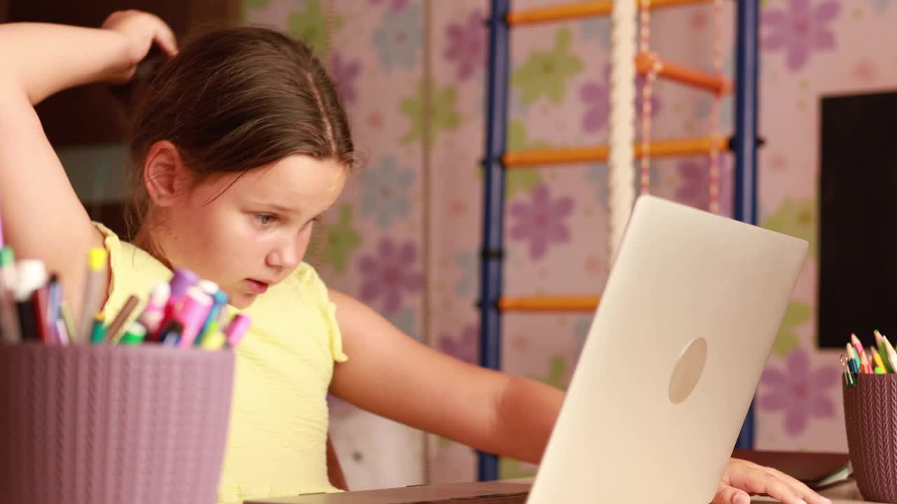 兴奋的青春期前的女孩，穿着黄色的裙子，坐在桌子旁看着笔记本电脑，同时学习投资的基本知识视频下载