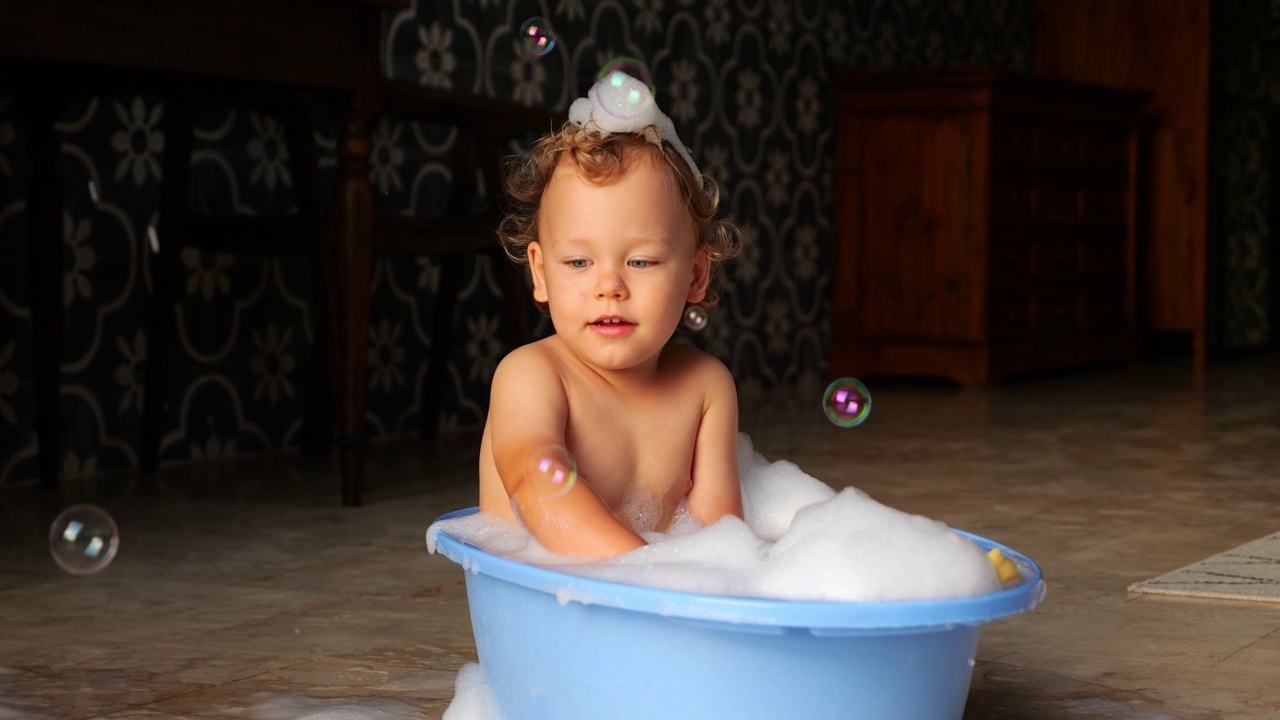 沉思的小男孩坐在小浴盆里，有热水，肥皂泡四处飞舞视频素材