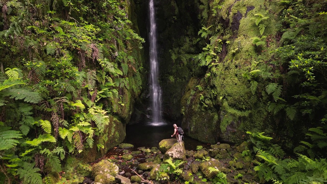 年轻的女性徒步旅行者在雨林的瀑布边。视频下载