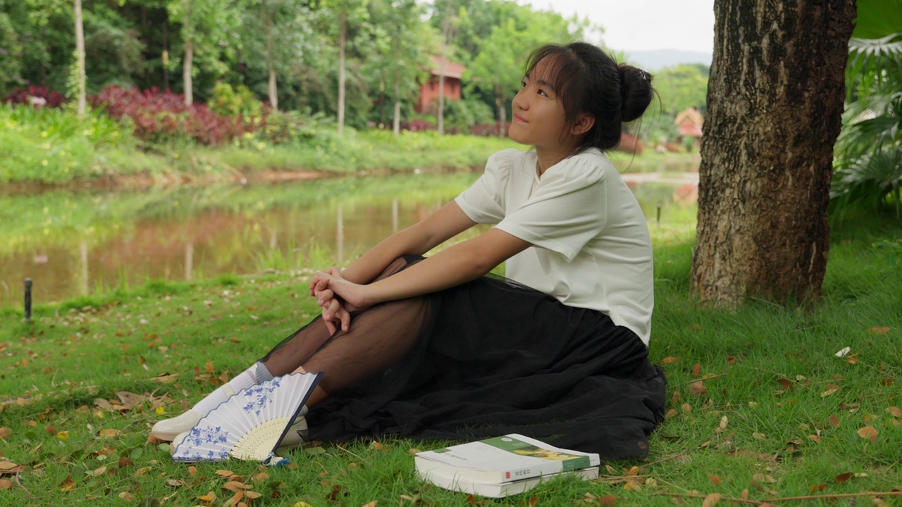 亚洲女孩在公园的树下读书视频下载