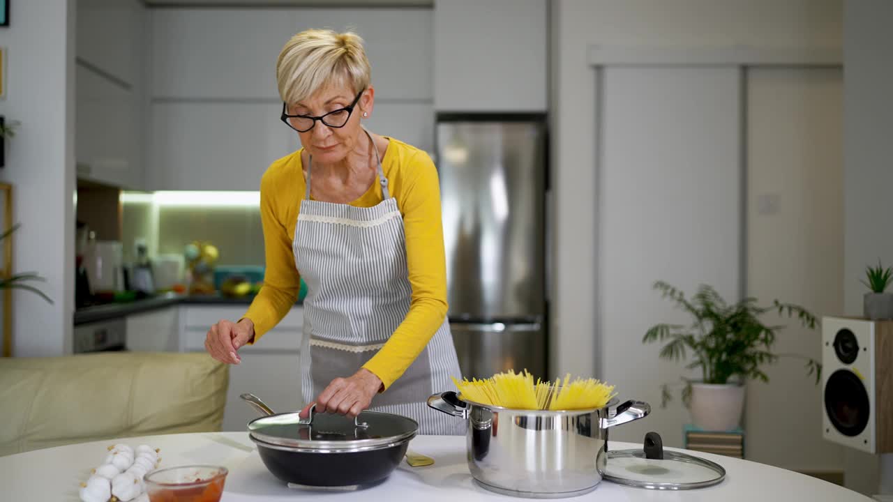 快乐的老妇人在她的现代厨房里做饭视频素材