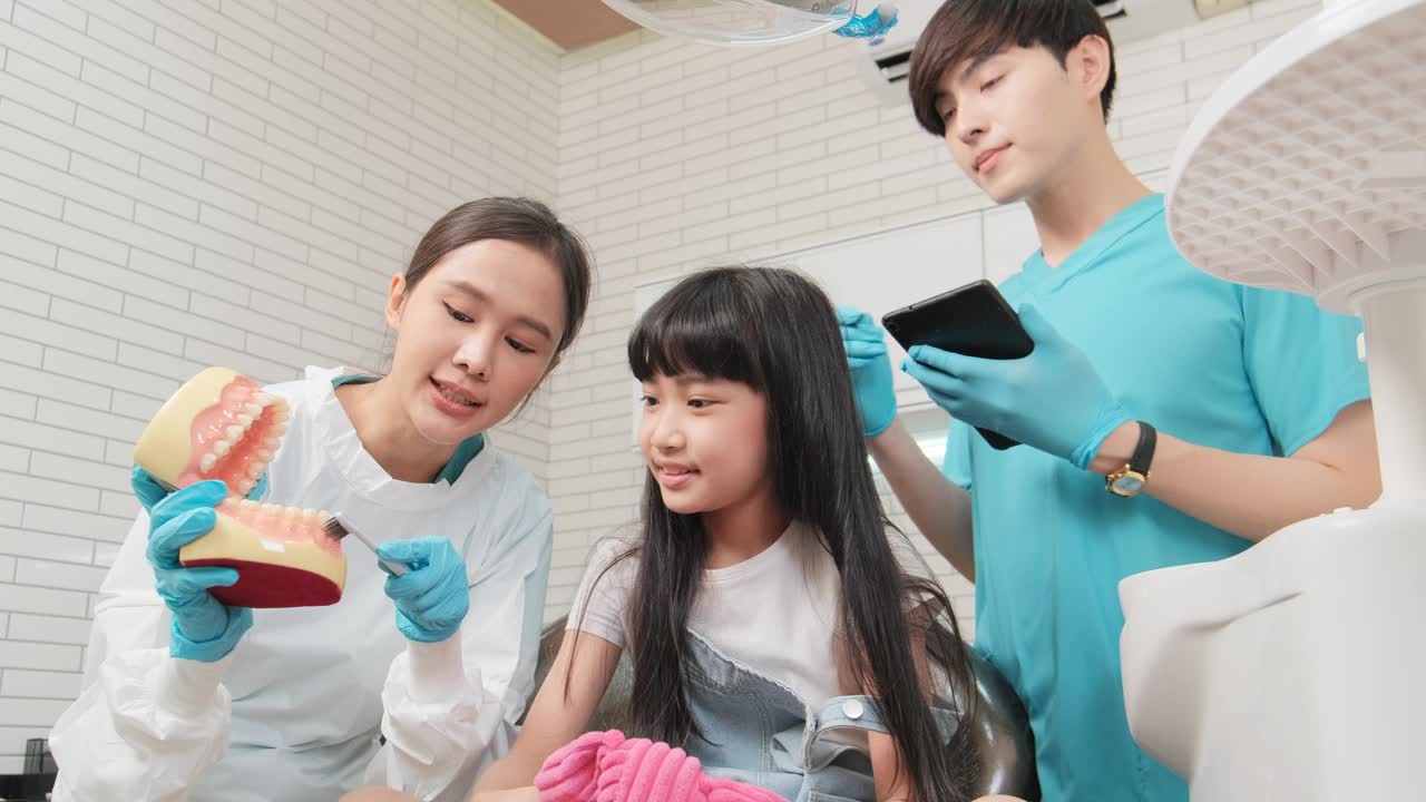 一位亚洲女牙医在牙科诊所向一个女孩展示牙刷。视频下载