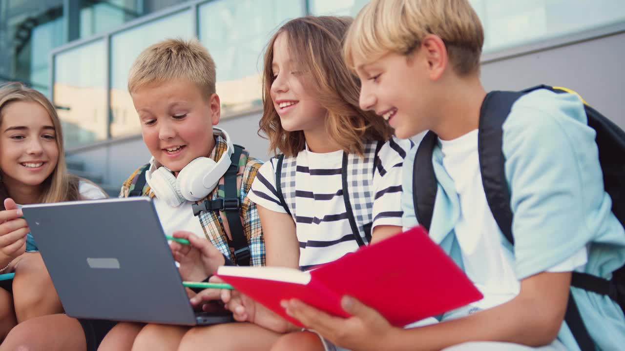 一群长相漂亮的现代女生和男生在学校大楼的背景下用笔记本电脑一起做一个项目。青少年的学习观念和生活方式。视频下载