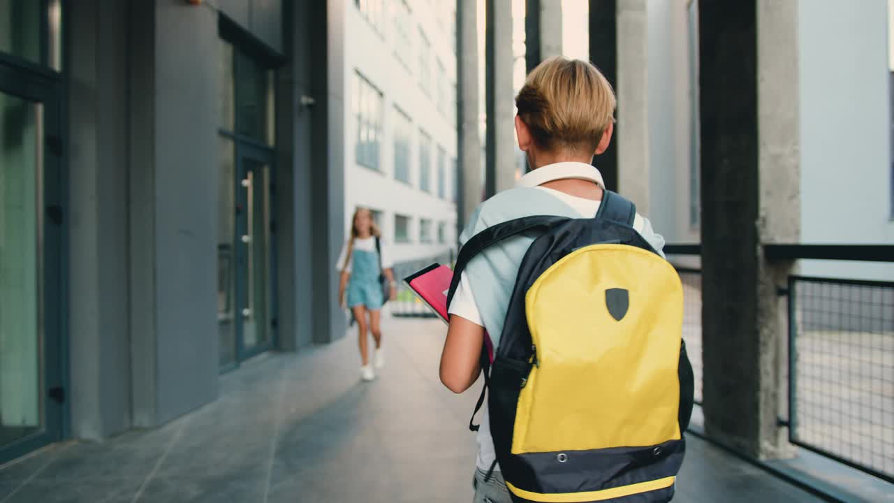 男生独自背着书包跑到现代学校大楼，一个同学去开会，女孩打招呼并击掌。视频下载