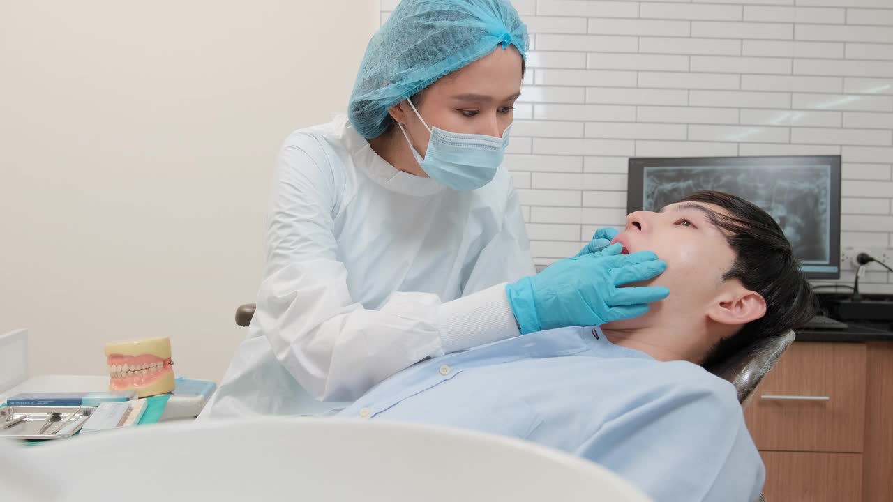 亚洲女牙医在牙科诊所检查年轻男性病人的牙齿。视频下载