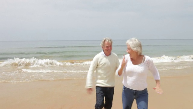 一对老年夫妇在秋季海滩上跑步视频素材