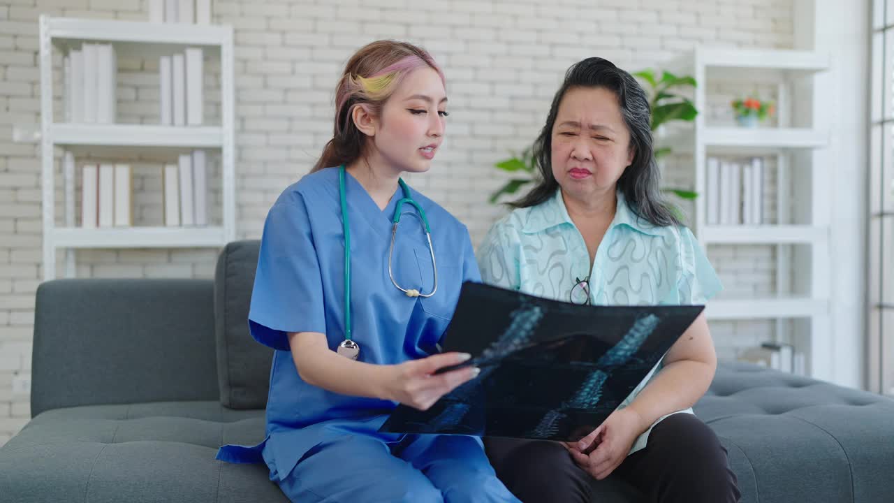 年轻的亚洲女医生向老年病人展示x光扫描，向诊所的妇女解释筛查胶片。老年妇女看完x光片后担心健康检查结果视频下载
