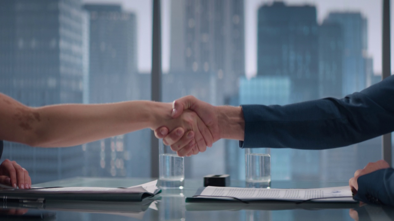 在摩天大楼办公室里，男女商业伙伴签署成功交易并握手的特写。公司首席执行官和投资经理就金融机会握手。视频下载