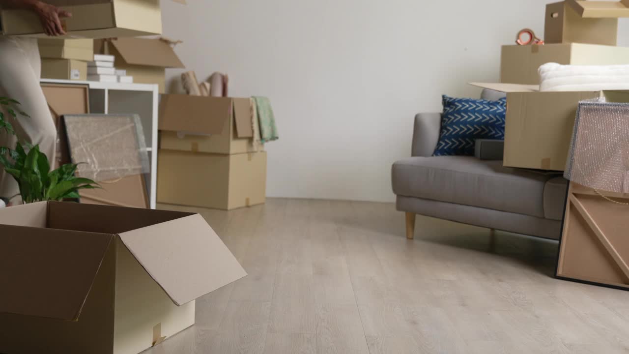年轻的亚洲女性搬进新公寓，用纸板箱拿着并打开她的物品。视频下载