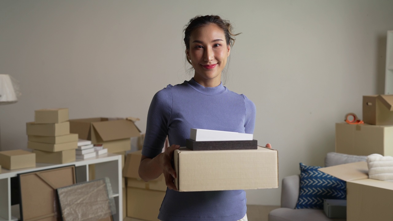 年轻的亚洲女人搬到新公寓，手里拿着装东西的纸板箱。视频下载