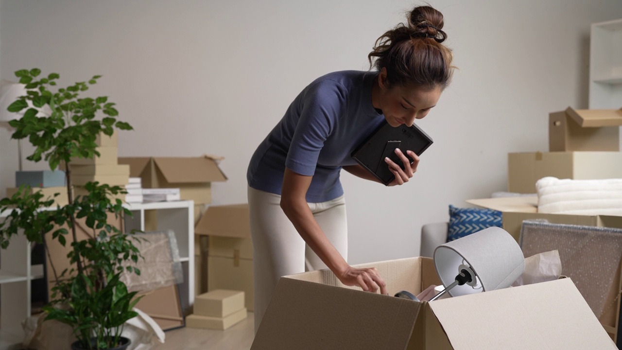 年轻的亚洲女性搬进新公寓，用纸板箱拿着并打开她的物品。视频下载