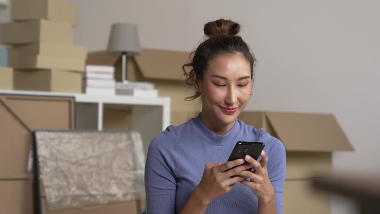 快乐的年轻亚洲女性搬到新家，坐在地板上玩智能手机。视频下载