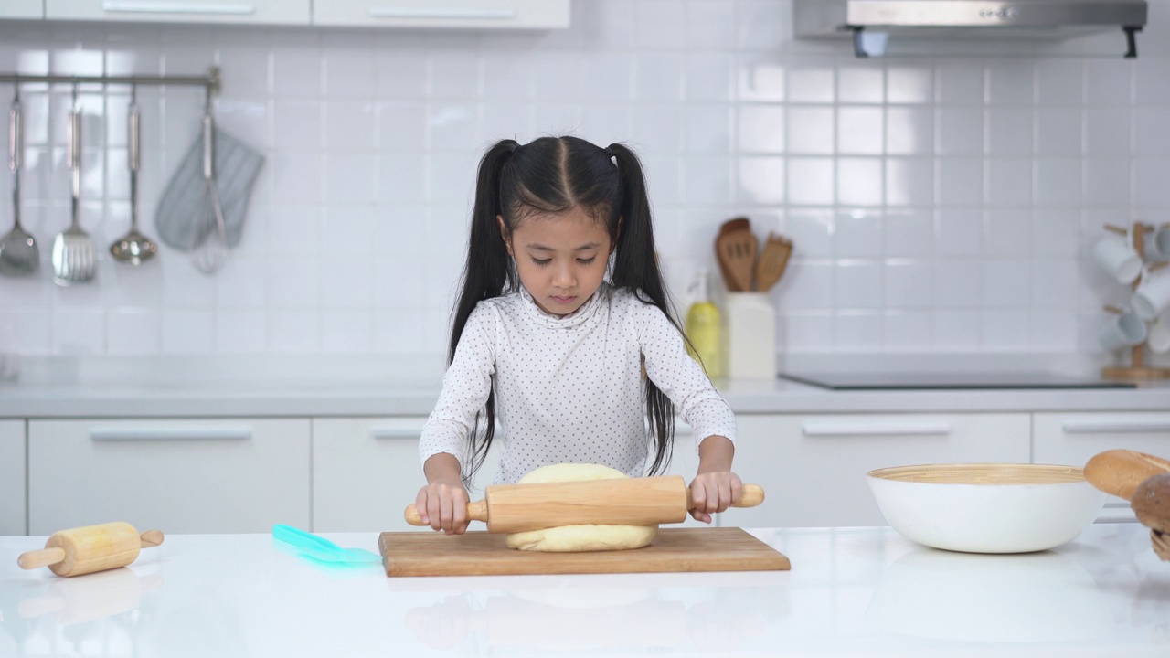 可爱的亚洲小女孩的肖像正在准备面团，在家里的现代厨房里烤饼干。儿童烹饪快乐活动家概念。视频下载