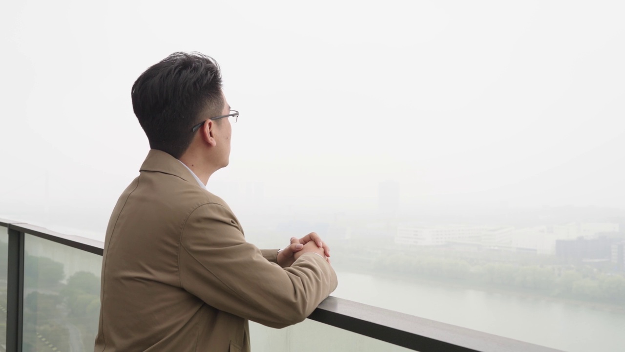 一位亚洲商人站在高层建筑的阳台上视频下载