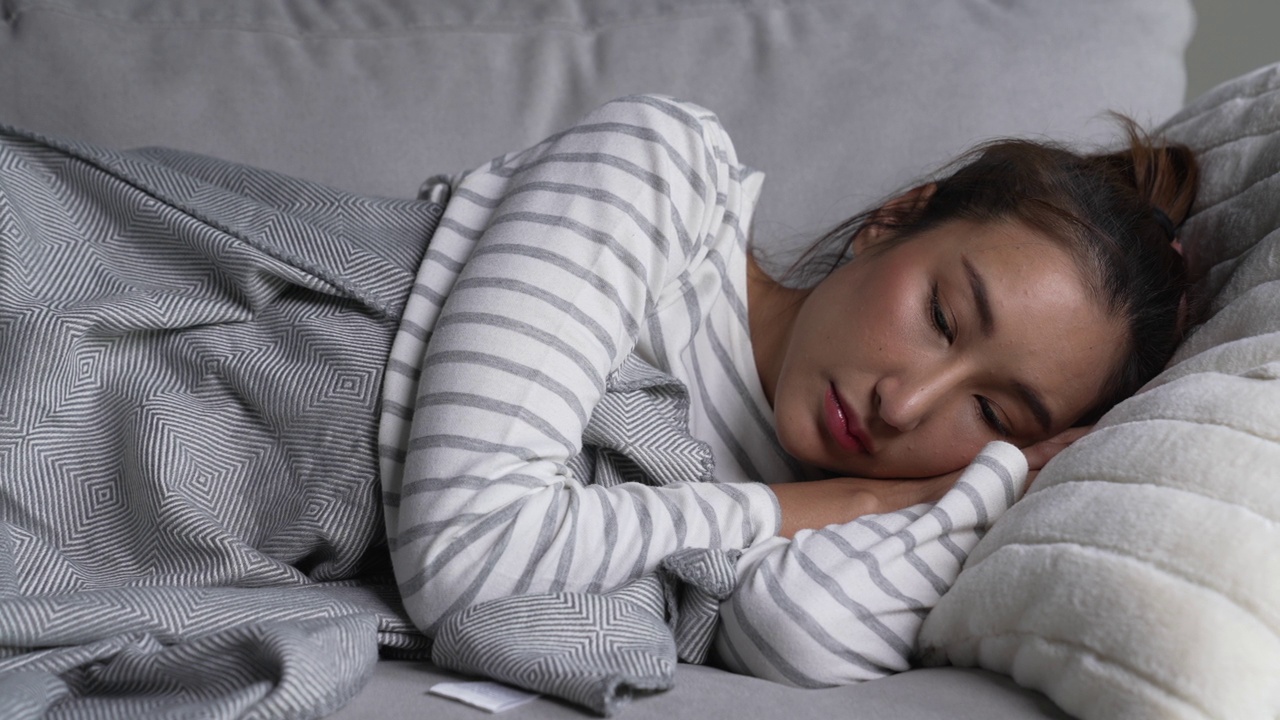 年轻的亚洲女子躺在家里的沙发上，感到悲伤、疲倦和担心，心理健康受到抑郁症的困扰。视频下载