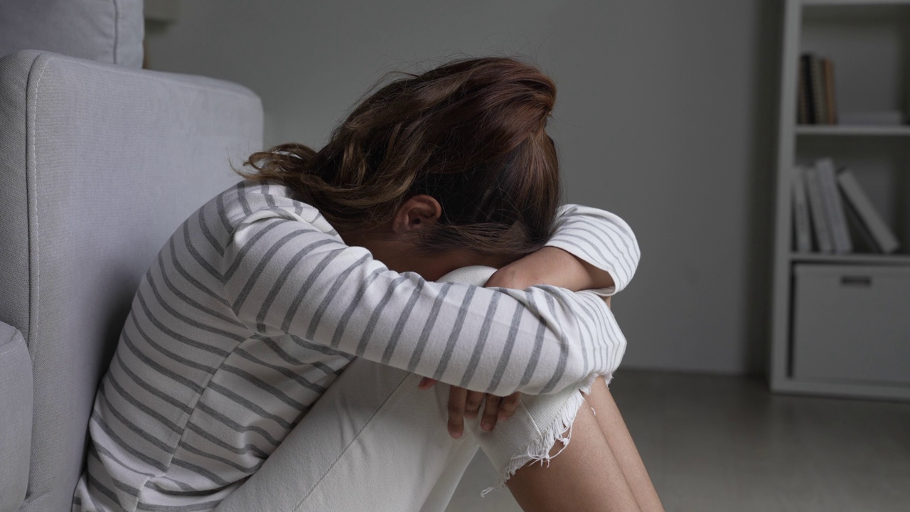 年轻的亚洲女子坐在地板上，感到悲伤、疲倦和担忧，心理健康状况堪忧。视频下载
