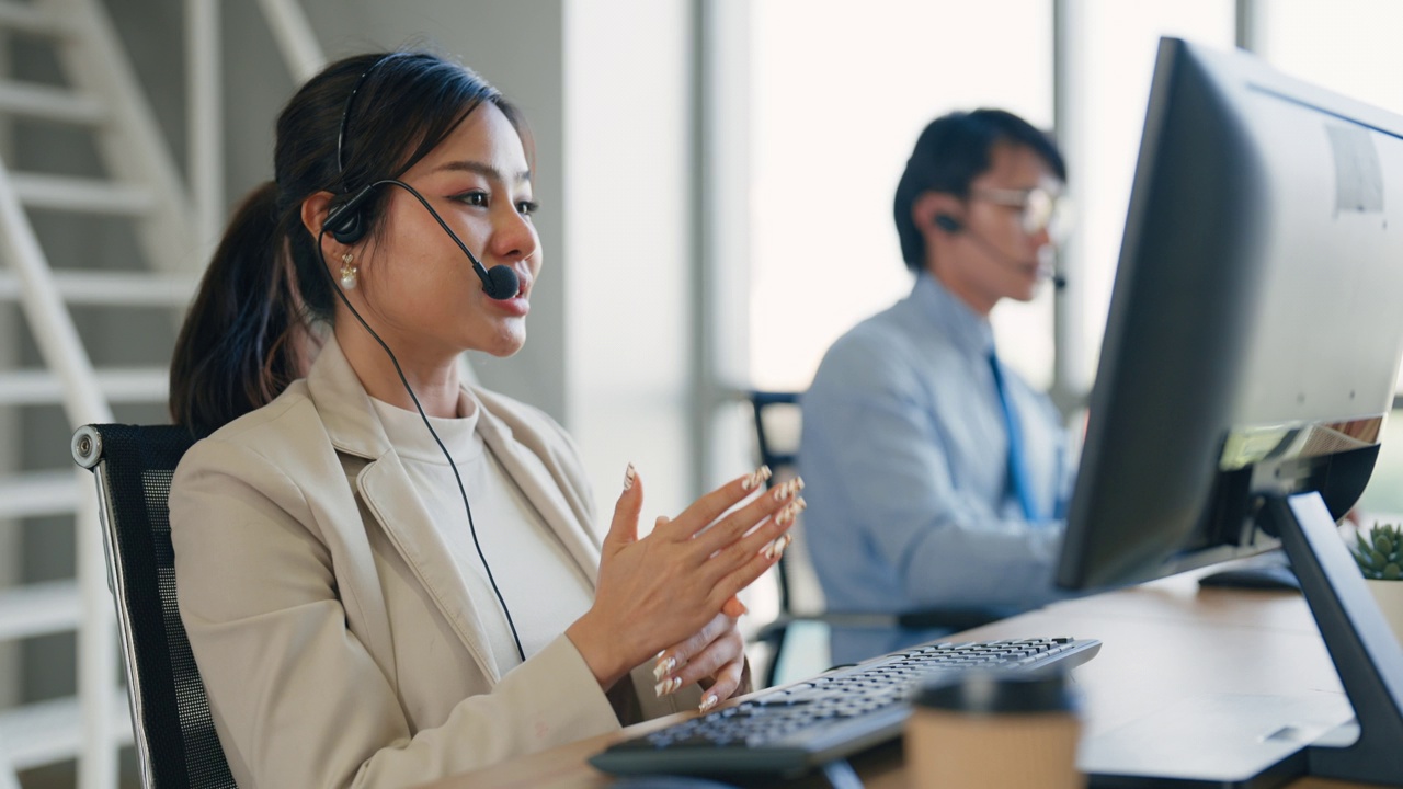 亚洲年轻成年女员工戴着耳机，在工作时间向客户咨询解决客户支持团队的问题。视频下载